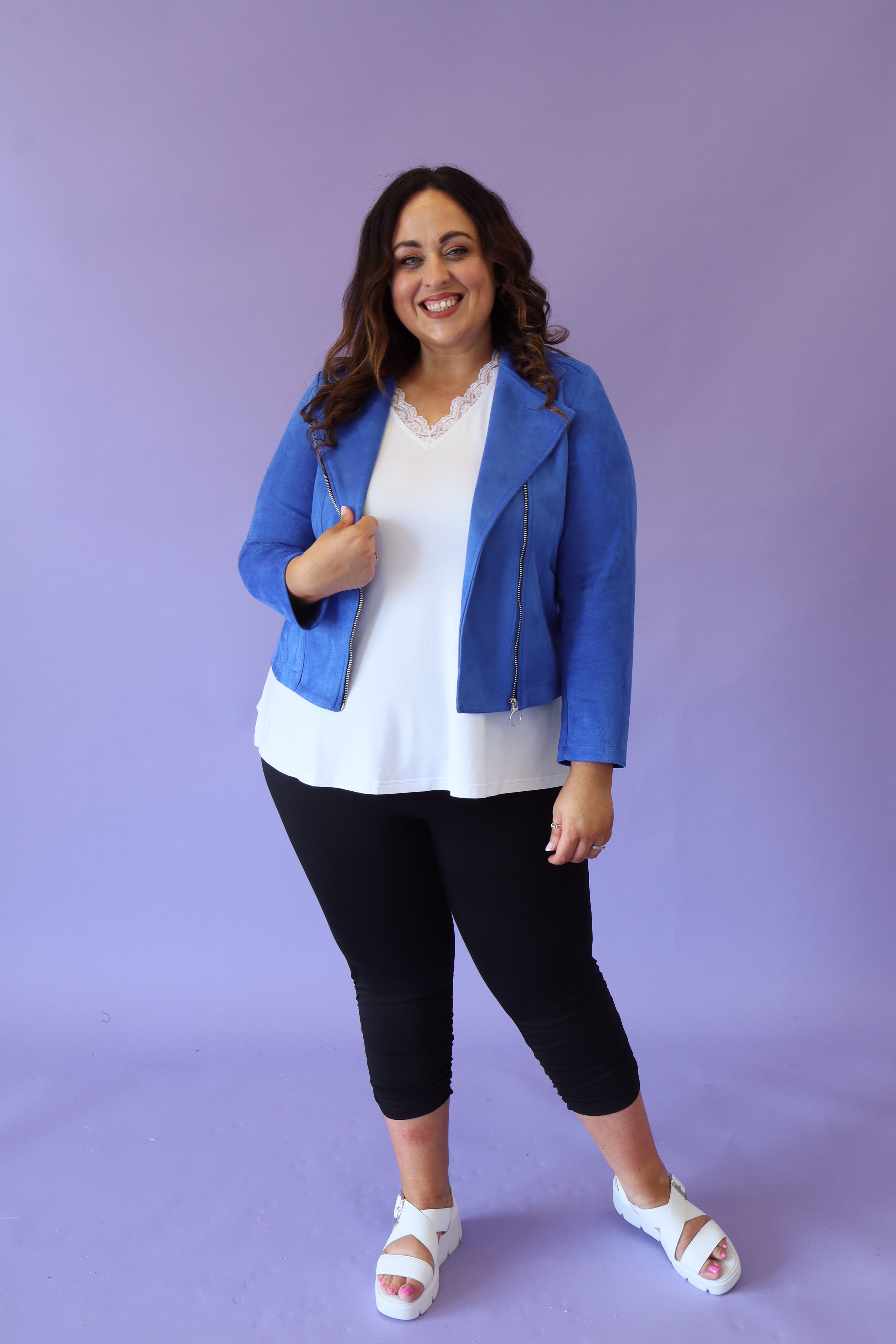 Person wearing a blue Amber jacket, white top, black pants, and sandals on a purple background