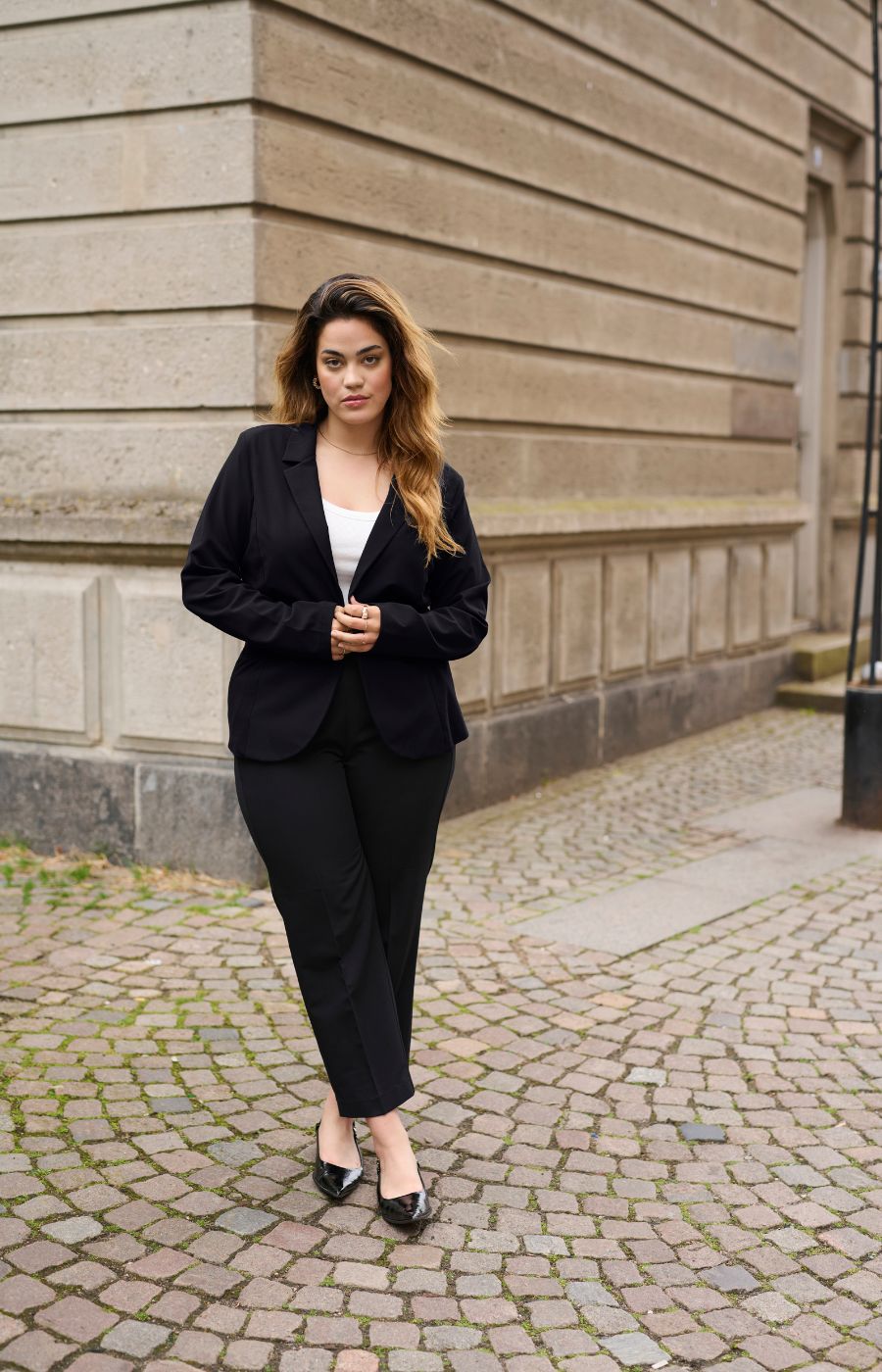 Woman in a black suit standing on a cobblestone street.