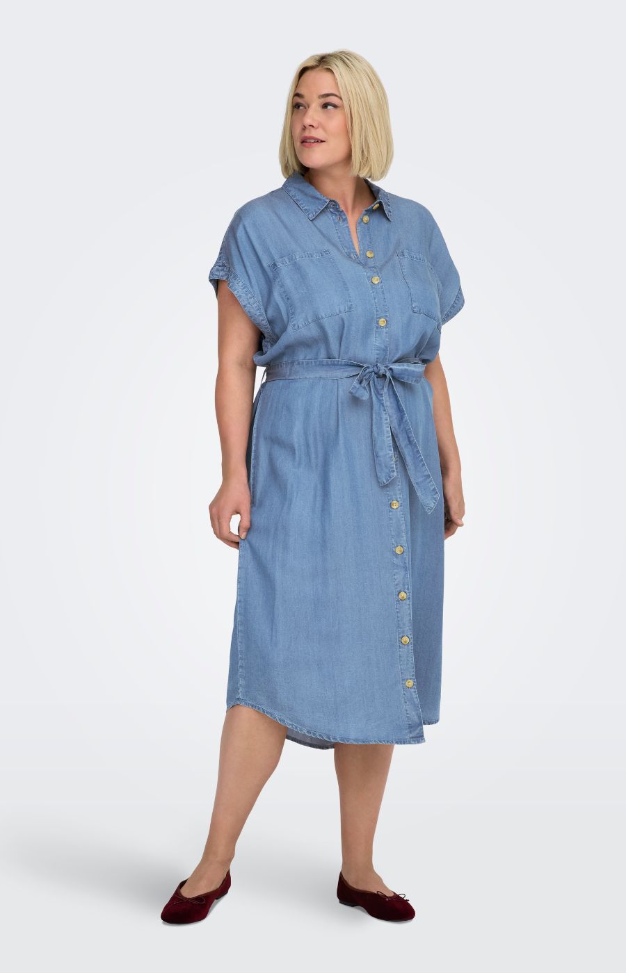 Woman wearing a blue dress, the Only Carmakoma Pema Denim Dress, with buttons on a white background