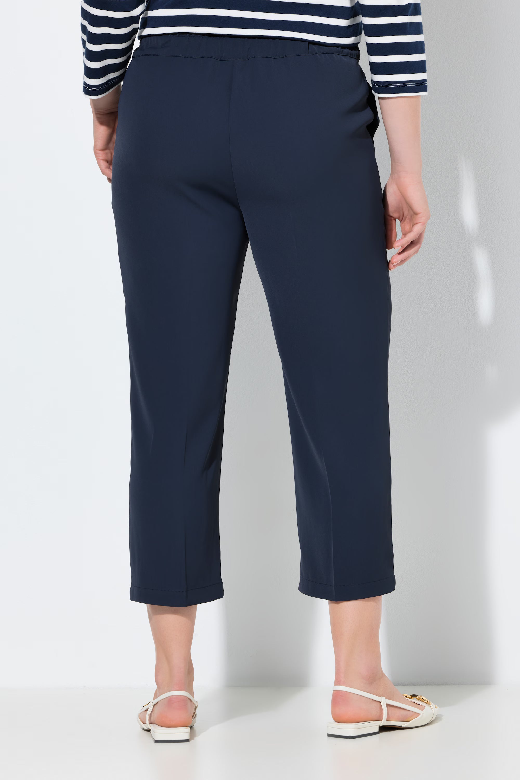 Back view of a women wearing the Ulla Popken 7/8th Trousers in Navy and a striped shirt on a white background