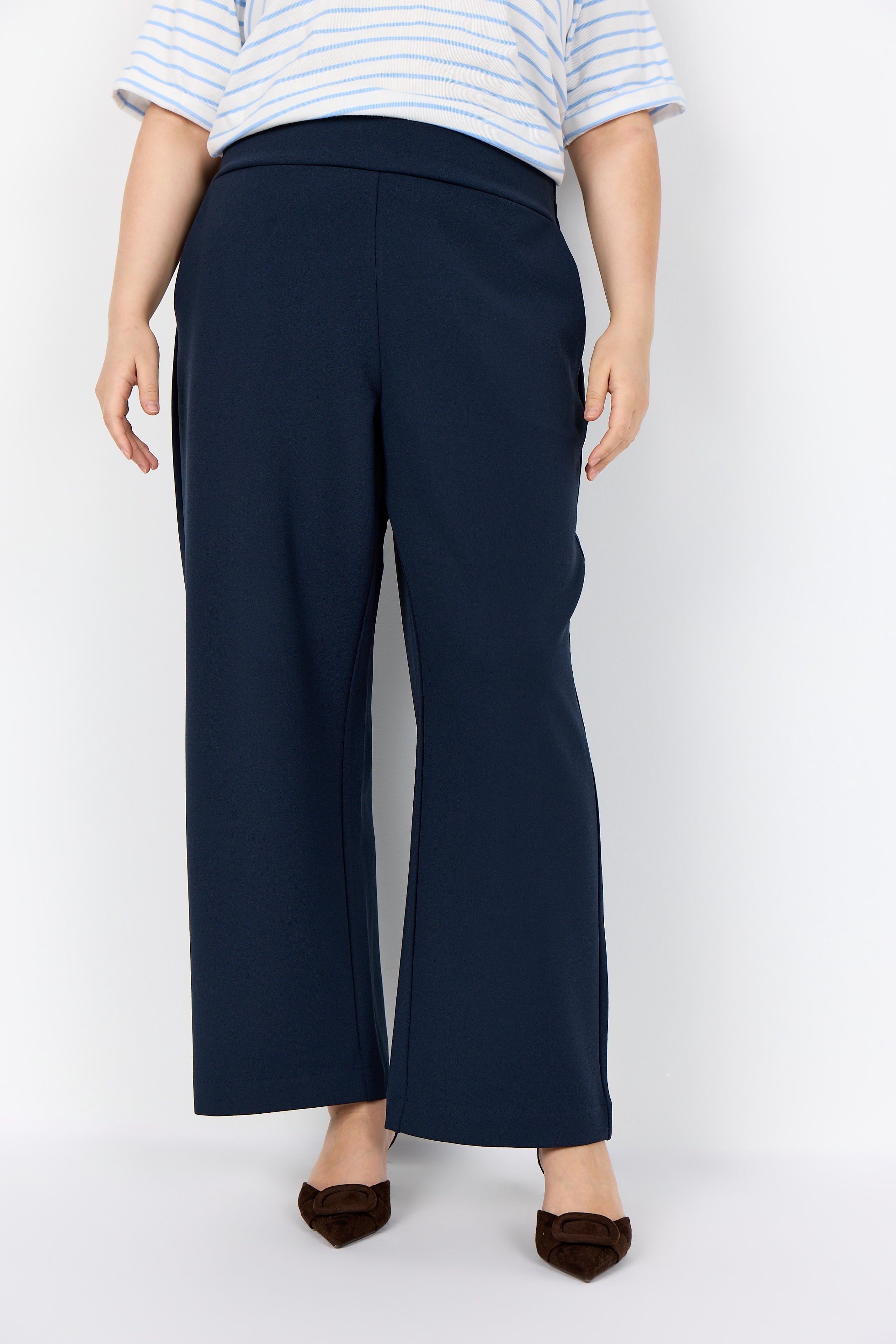 Person wearing the Wasabi Kufa Trousers in Navy, a navy wide-leg  trousers and a striped shirt on a white background