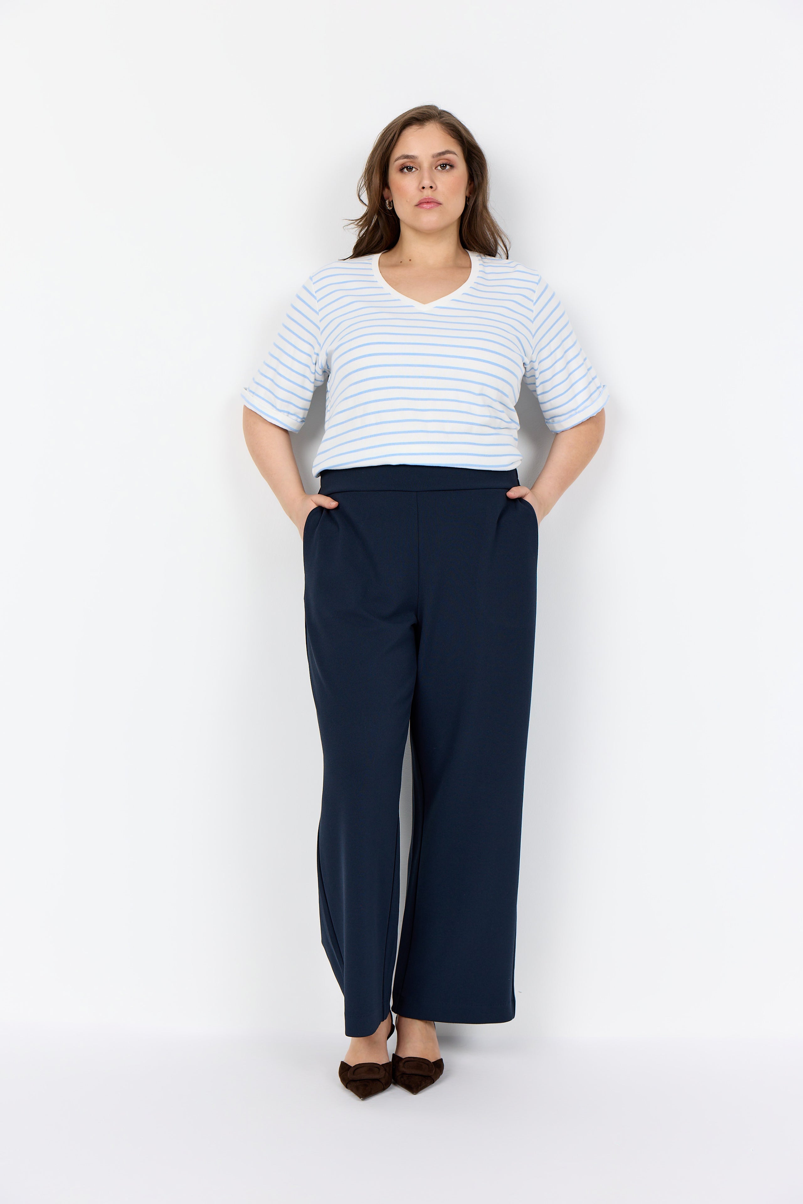 Person wearing the Wasabi Kufa Trousers in Navy, a navy wide-leg  trousers and a striped shirt on a white background 
